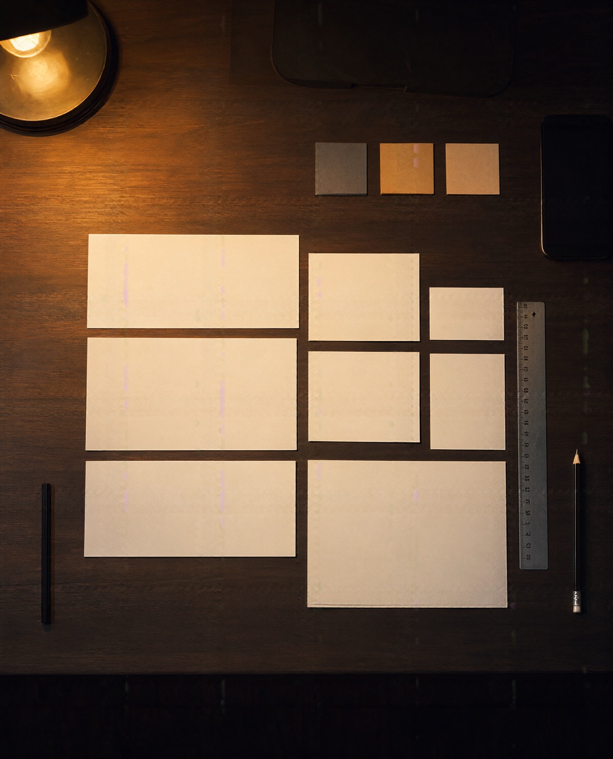 Blank paper cards in a careful grid with colour swatches and a pencil on a walnut desk under an amber lamp.