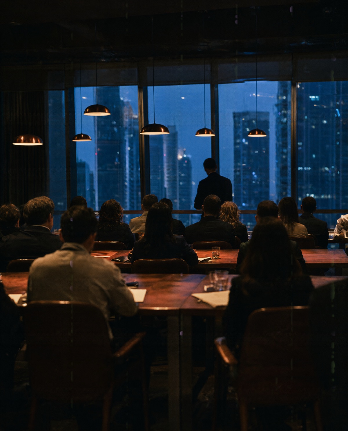 Professionals at walnut tables in an executive seminar high above Dubai, a presenter in silhouette by the window.